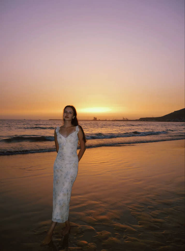 Woman in a white dress standing on a beach at sunset.