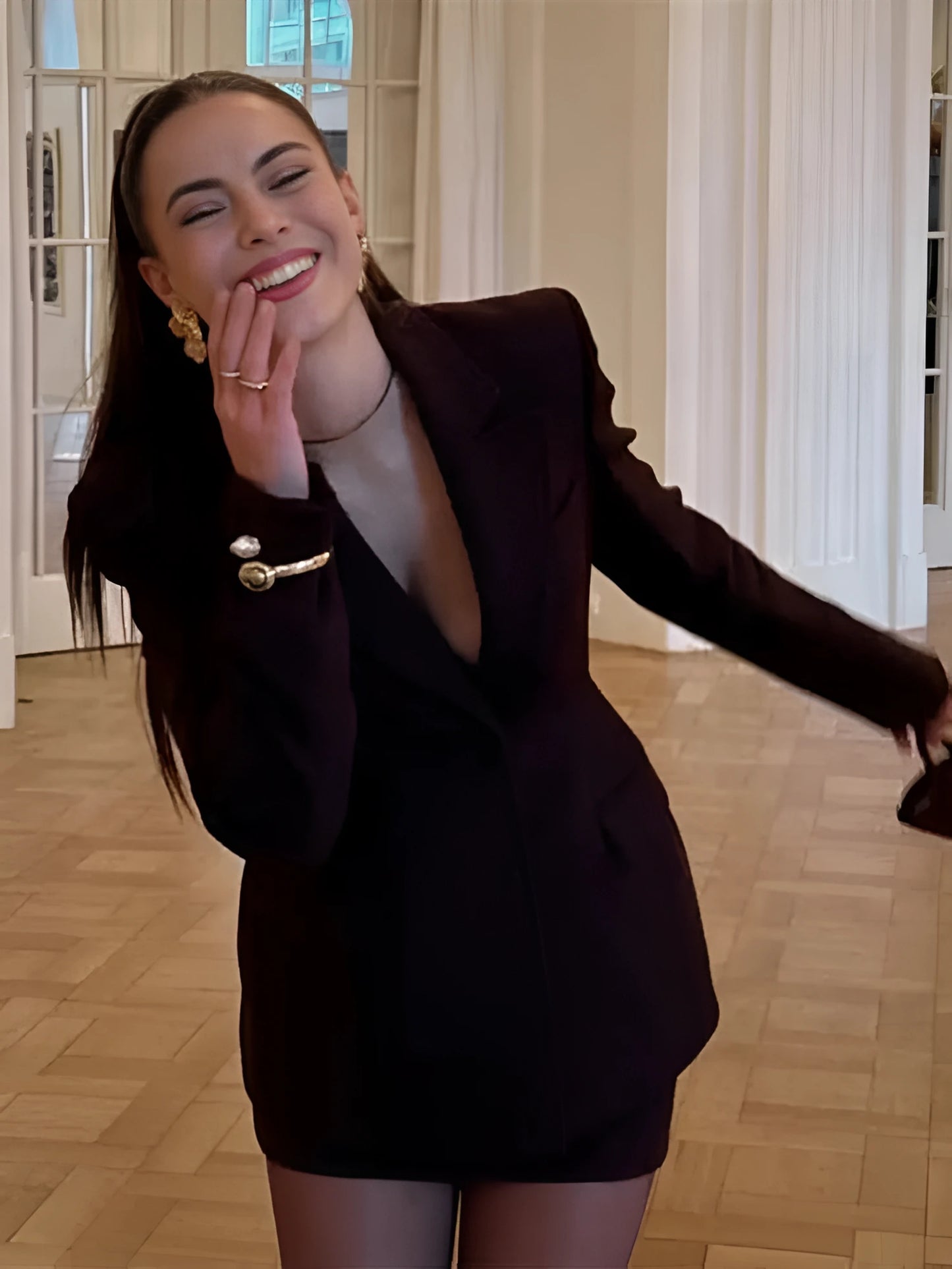 Woman wearing a slim-fit brown blazer jacket and A-line mini skirt in an office setting, confidently presenting in a modern workspace.