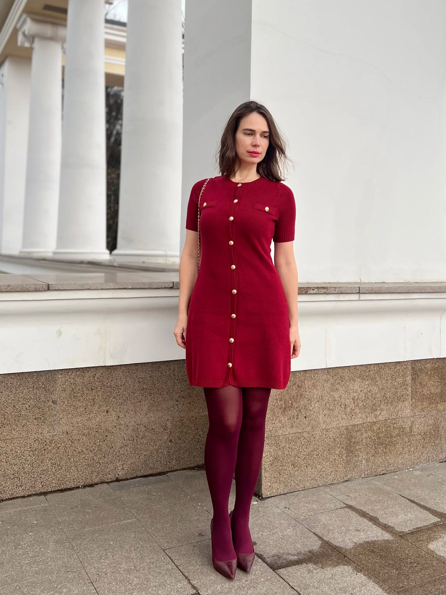 Confident woman walking downtown in a fitted ribbed knit mini dress with metal buttons, styled with sunglasses and ankle boots.