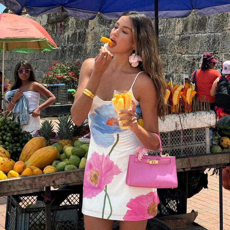 Woman in a floral dress eating fruit at an outdoor market.