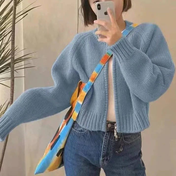 Person wearing a blue sweater and jeans, holding a colorful bag.