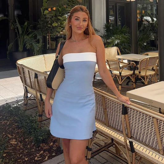 Woman wearing a strapless A-line mini dress at a rooftop party, holding a clutch and cocktail.