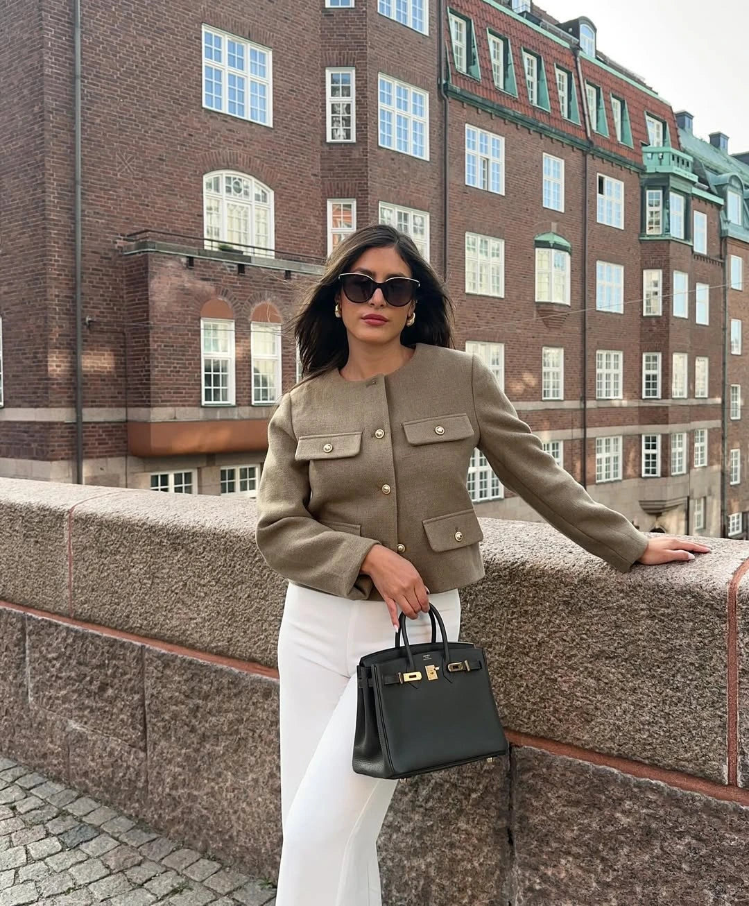 The woman looks casual and chic while walking around the city in a lightly cut khaki double-breasted tweed jacket with buttons.