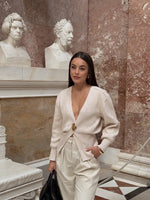 Model wearing a V-neck knit cardigan over a white tank top and trousers, enjoying a coffee outdoors in spring.