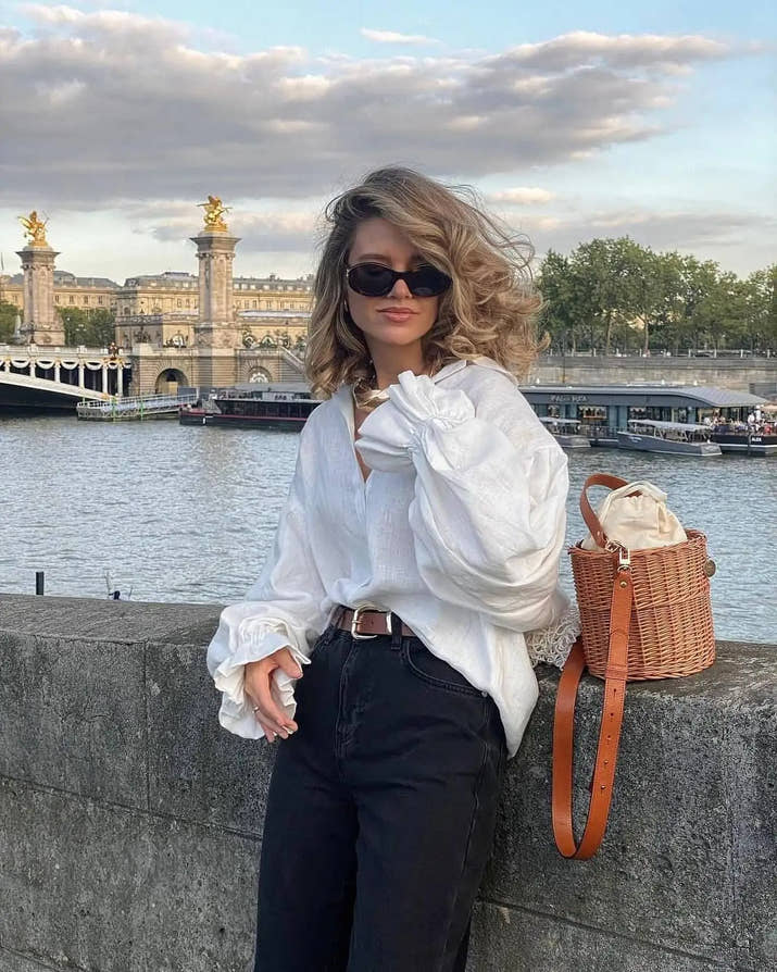 Model wearing white puff sleeve blouse with denim shorts, standing outdoors on a sunny day.