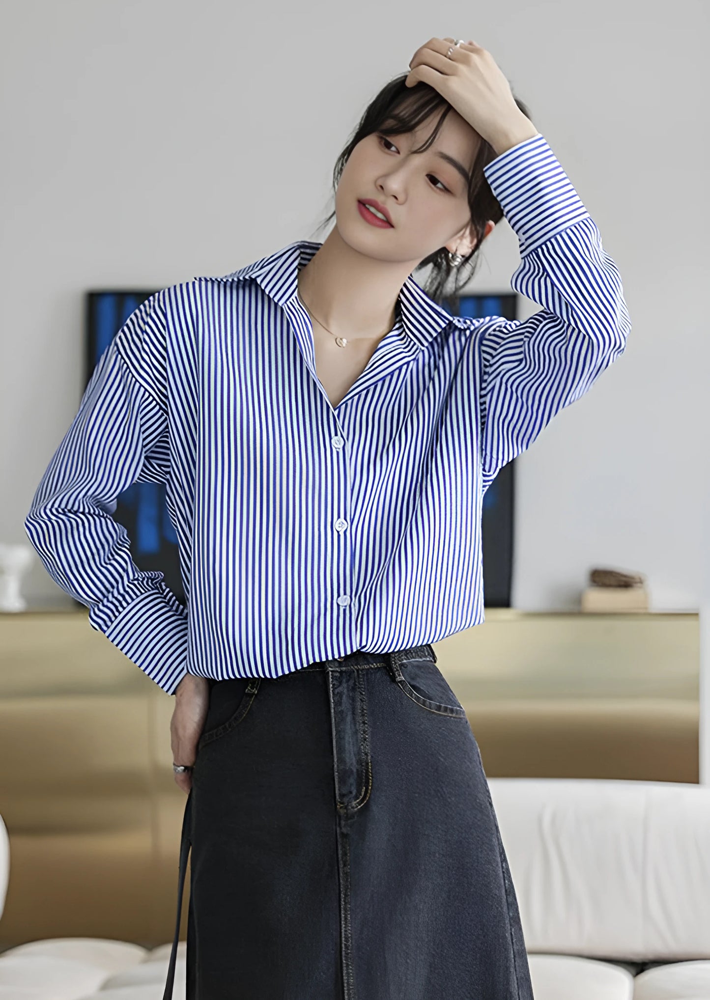 Woman wearing a blue-white striped loose office shirt with lantern sleeves in a minimalist urban setting.