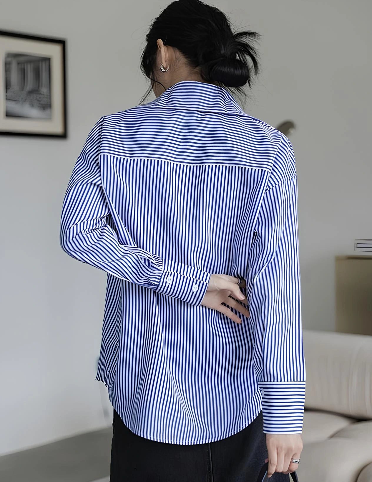 Woman wearing a blue-white striped loose office shirt with lantern sleeves in a minimalist urban setting.