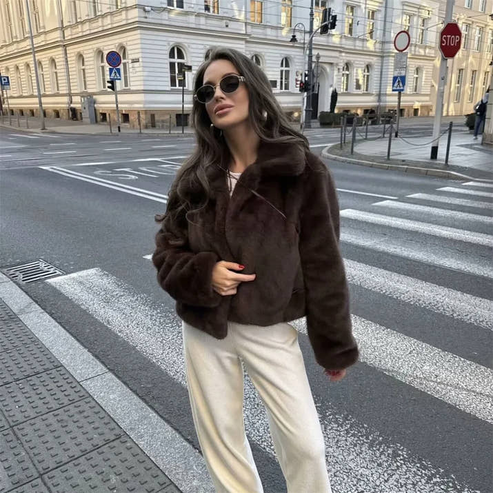 Woman wearing a brown faux fur winter jacket while sipping coffee outside a cozy café in cold weather.