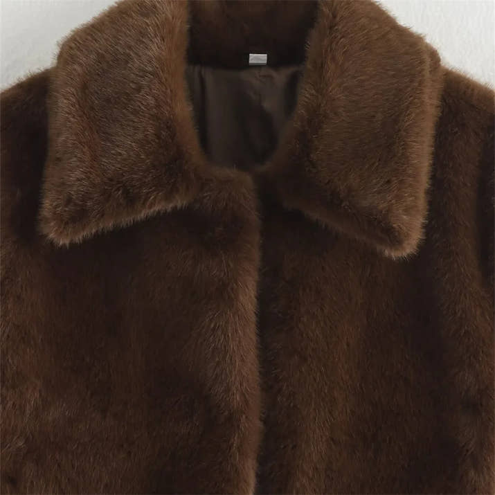 Woman wearing a brown faux fur winter jacket while sipping coffee outside a cozy café in cold weather.