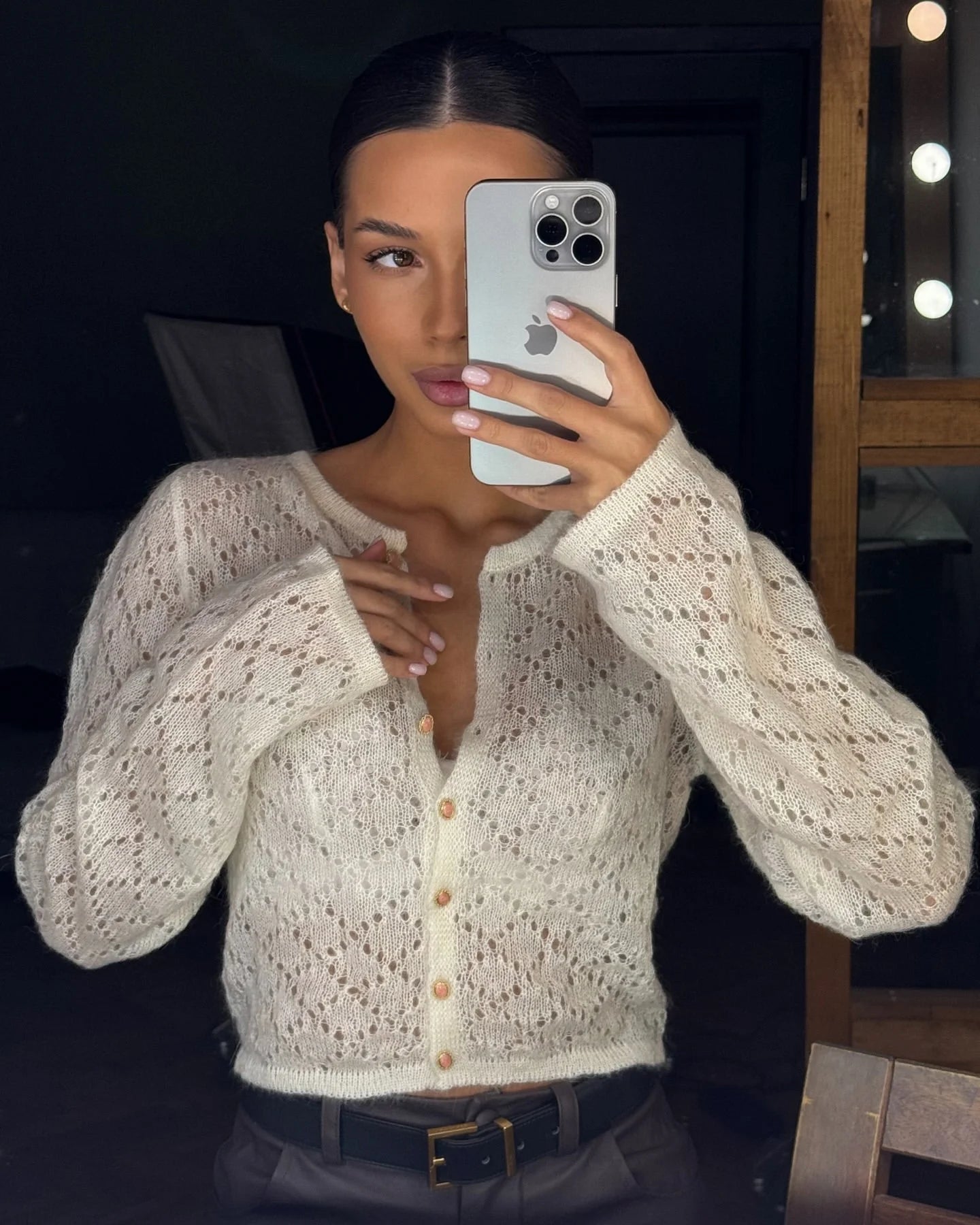 Person wearing a white lace cardigan with buttons, taking a mirror selfie.