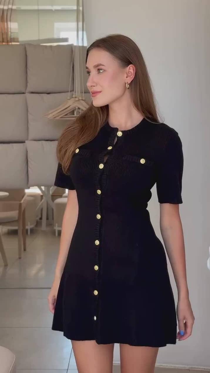 Confident woman walking downtown in a fitted ribbed knit mini dress with metal buttons, styled with sunglasses and ankle boots.