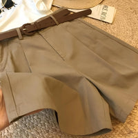 Woman wearing high-waisted cotton shorts with a tucked-in blouse, walking outdoors in summer.