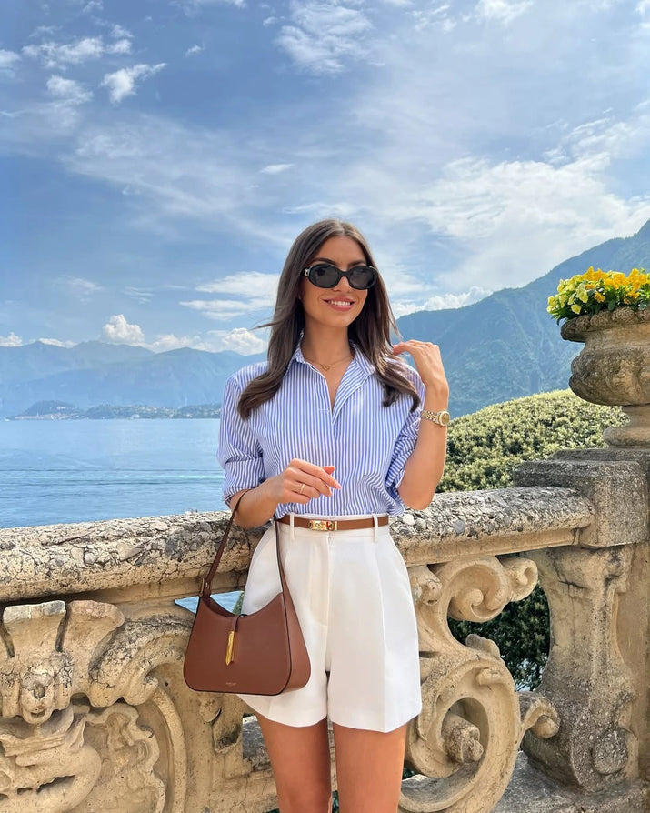 Woman wearing high-waisted cotton shorts with a tucked-in blouse, walking outdoors in summer.