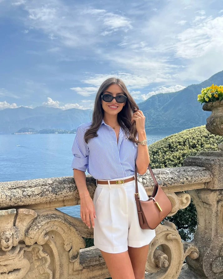 Woman wearing high-waisted cotton shorts with a tucked-in blouse, walking outdoors in summer.