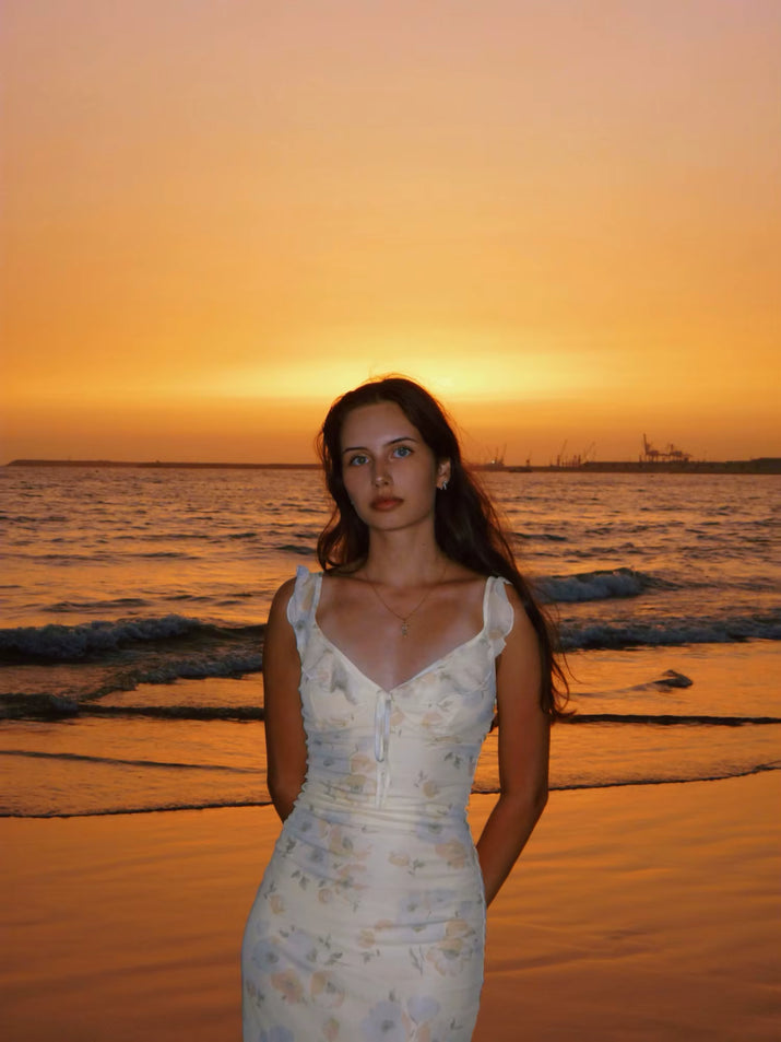 Woman in a floral dress standing on a beach at sunset