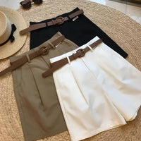 Woman wearing high-waisted cotton shorts with a tucked-in blouse, walking outdoors in summer.