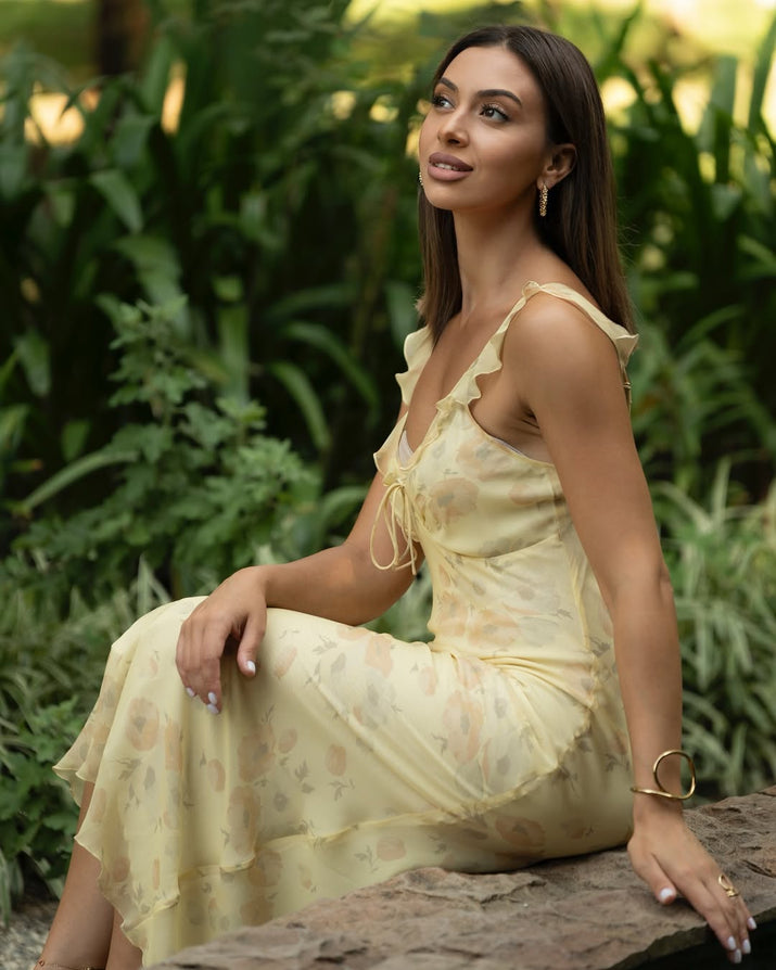 Woman in a light yellow dress sitting on a rock with greenery in the background