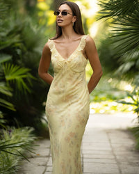 Woman in a light yellow dress standing in a lush green garden