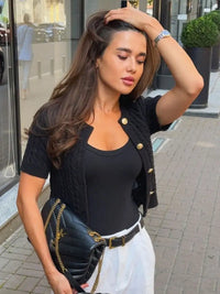 Woman in black top and cardigan with white pants on a city street