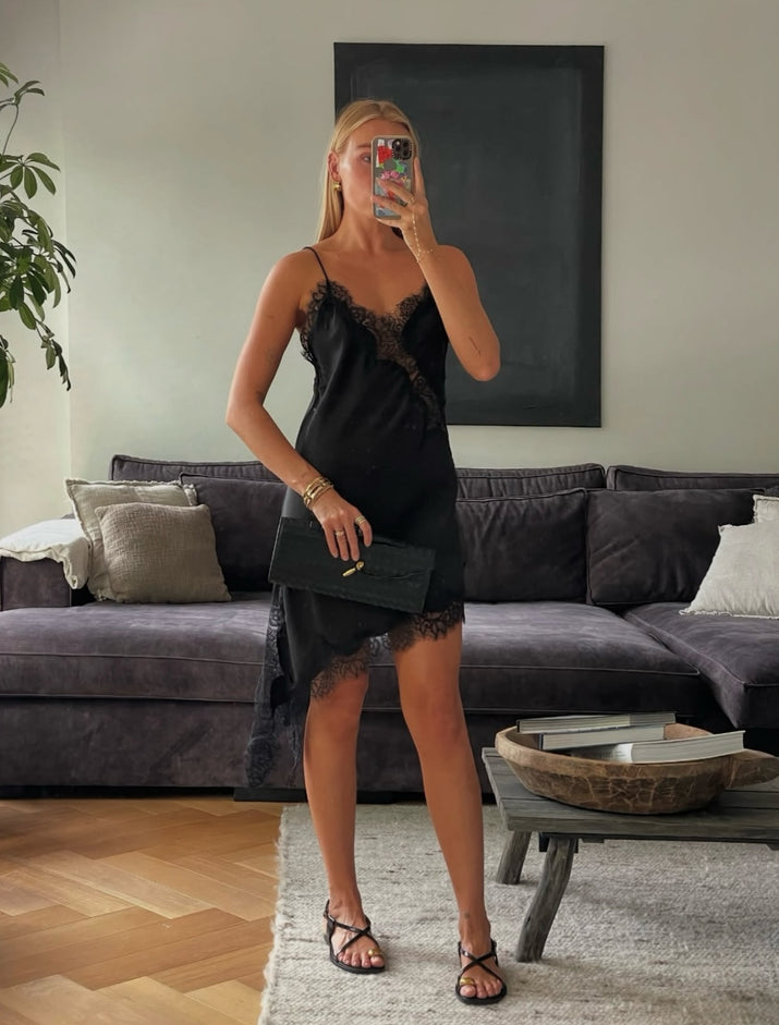 Woman taking a mirror selfie in a black lace dress in a living room.