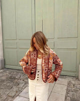 Woman walking outdoors in fall wearing a quilted patchwork floral jacket in orange tones.