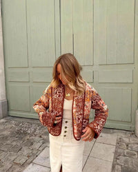 Woman walking outdoors in fall wearing a quilted patchwork floral jacket in orange tones.