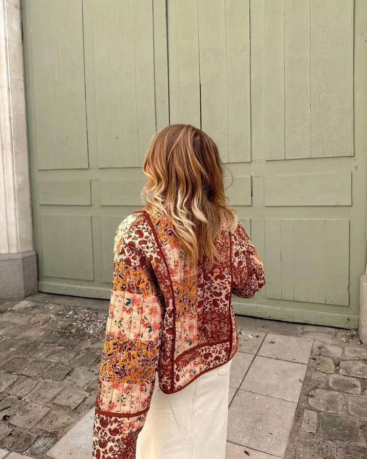 Woman walking outdoors in fall wearing a quilted patchwork floral jacket in orange tones.