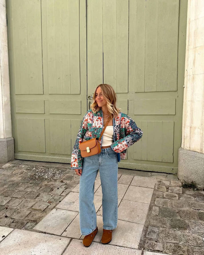 Woman walking outdoors in fall wearing a quilted patchwork floral jacket in orange tones.