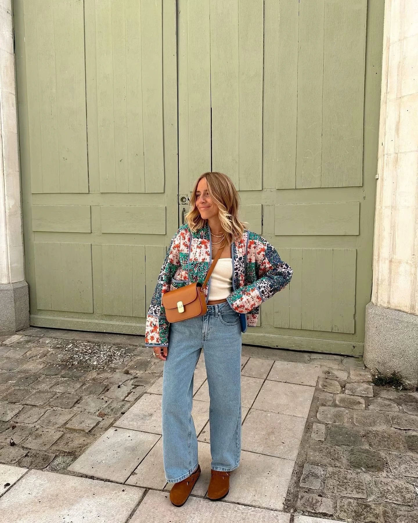 Woman walking outdoors in fall wearing a quilted patchwork floral jacket in orange tones.
