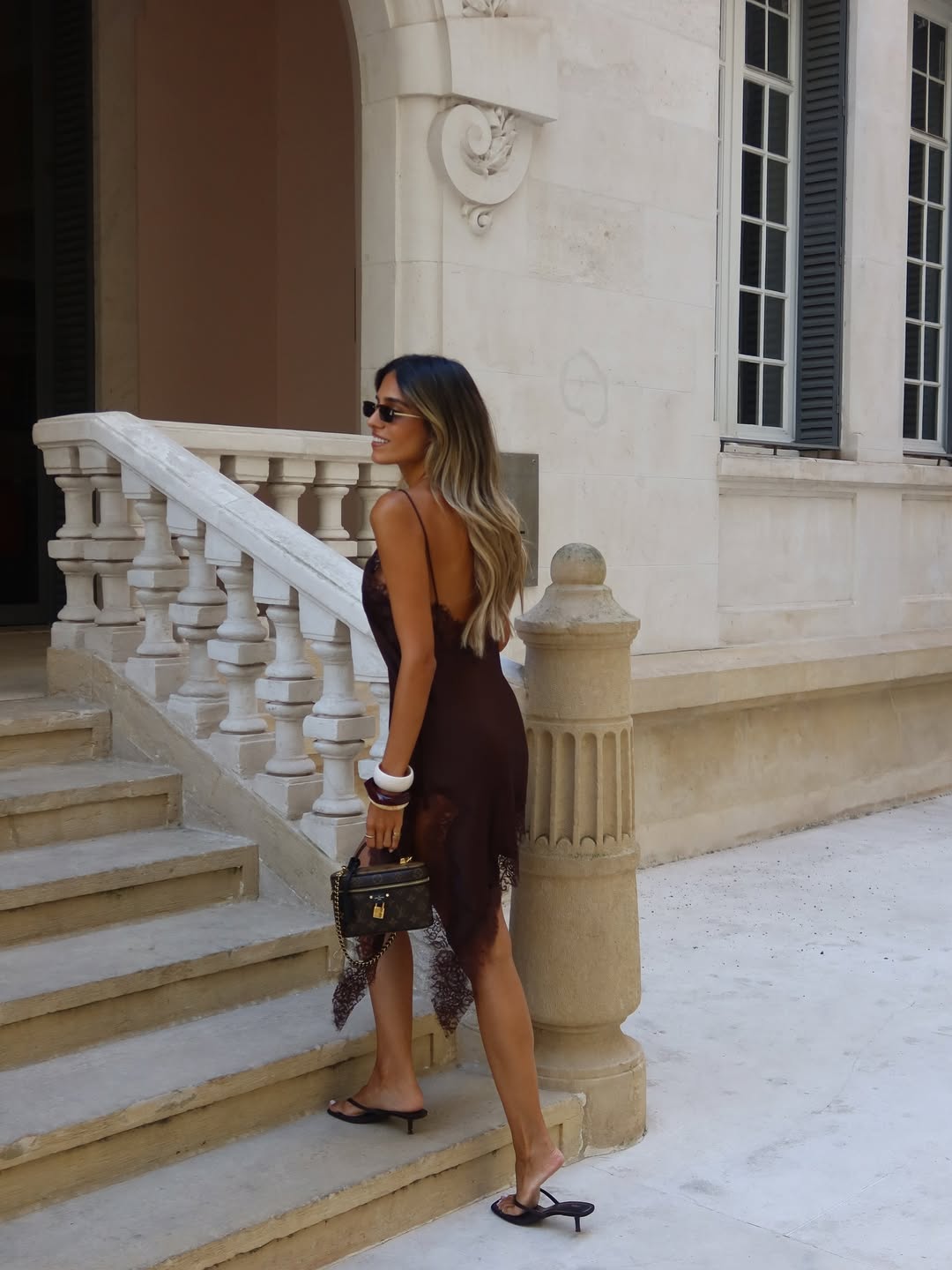 Woman in a brown dress standing on stone steps in front of a building