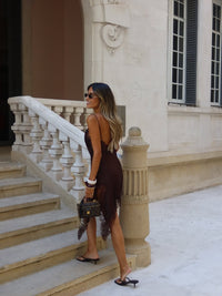 Woman in a brown dress standing on stone steps in front of a building