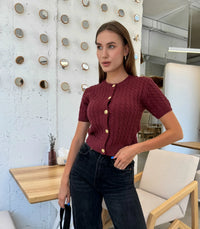 Woman wearing a maroon knitted cardigan with gold buttons in an indoor setting.