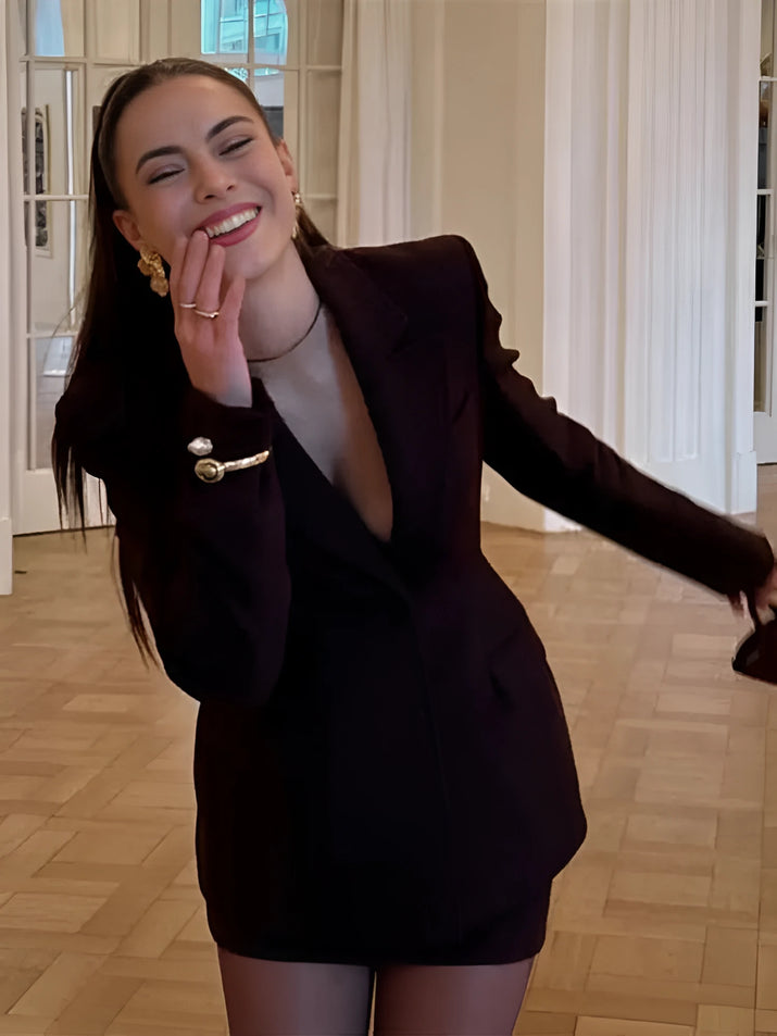 Woman wearing a slim-fit brown blazer jacket and A-line mini skirt in an office setting, confidently presenting in a modern workspace.