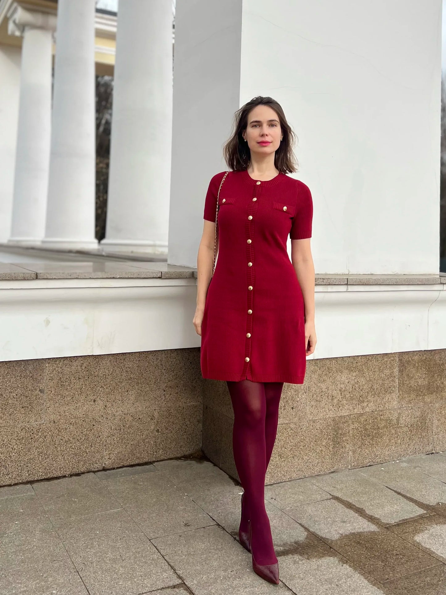 Confident woman walking downtown in a fitted ribbed knit mini dress with metal buttons, styled with sunglasses and ankle boots.