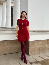Confident woman walking downtown in a fitted ribbed knit mini dress with metal buttons, styled with sunglasses and ankle boots.