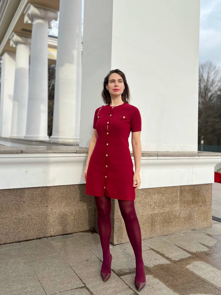 Confident woman walking downtown in a fitted ribbed knit mini dress with metal buttons, styled with sunglasses and ankle boots.