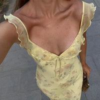 Woman wearing a light yellow floral dress with ruffled sleeves on a pavement background