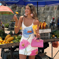 Woman in a floral dress holding fruit at an outdoor market.