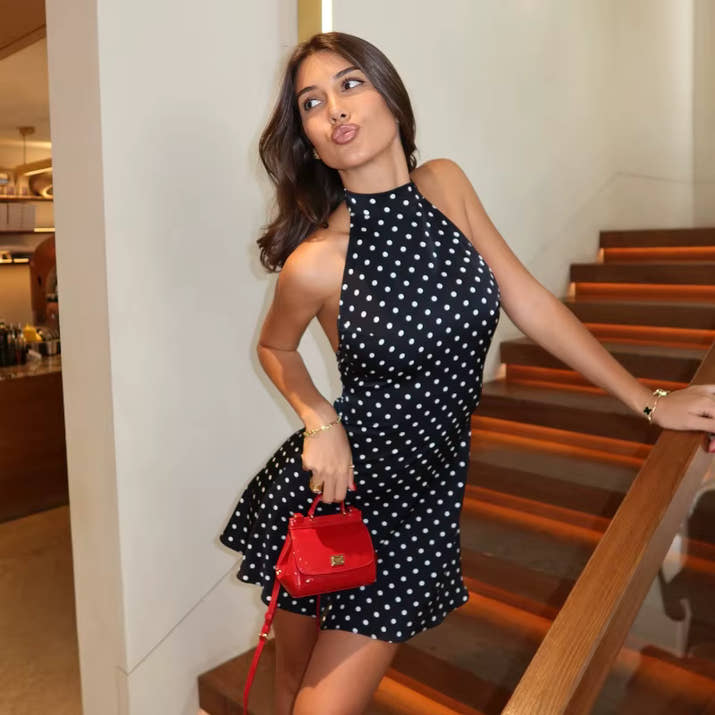 Woman in a black polka dot dress holding a red handbag on a staircase.