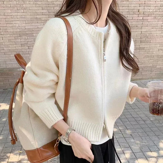 Person wearing a beige sweater with a brown leather bag against a brick wall.