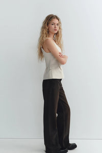Woman wearing a beige sleeveless V-neck crop top with ruffled detail and zipper, styled casually in a café setting.