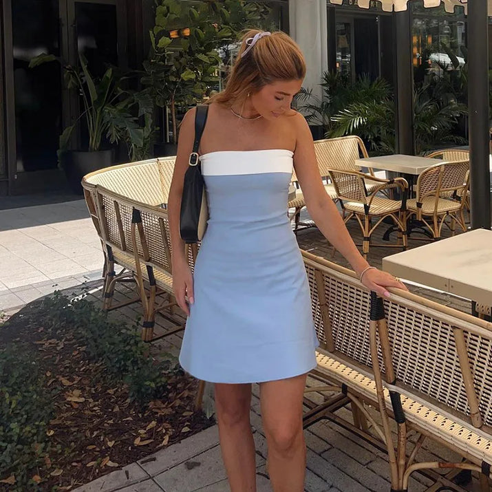 Woman wearing a strapless A-line mini dress at a rooftop party, holding a clutch and cocktail.