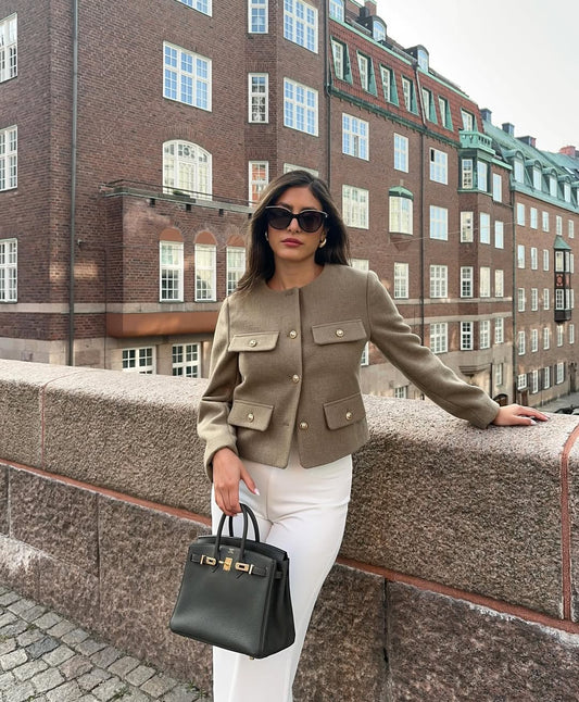 The woman looks casual and chic while walking around the city in a lightly cut khaki double-breasted tweed jacket with buttons.