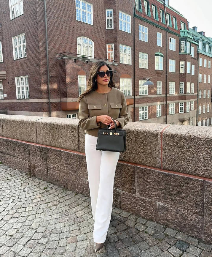 The woman looks casual and chic while walking around the city in a lightly cut khaki double-breasted tweed jacket with buttons.