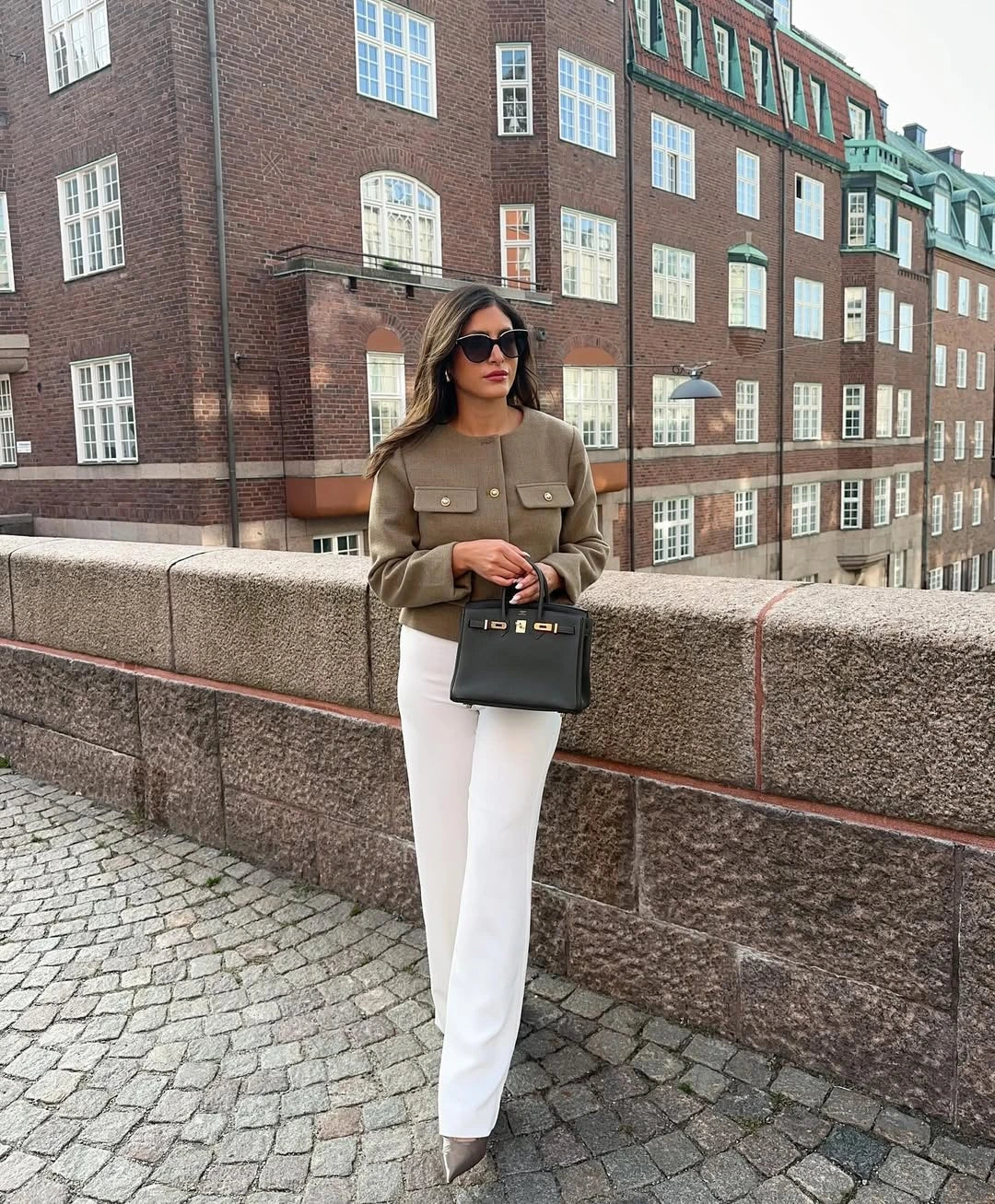 The woman looks casual and chic while walking around the city in a lightly cut khaki double-breasted tweed jacket with buttons.