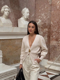 Model wearing a V-neck knit cardigan over a white tank top and trousers, enjoying a coffee outdoors in spring.