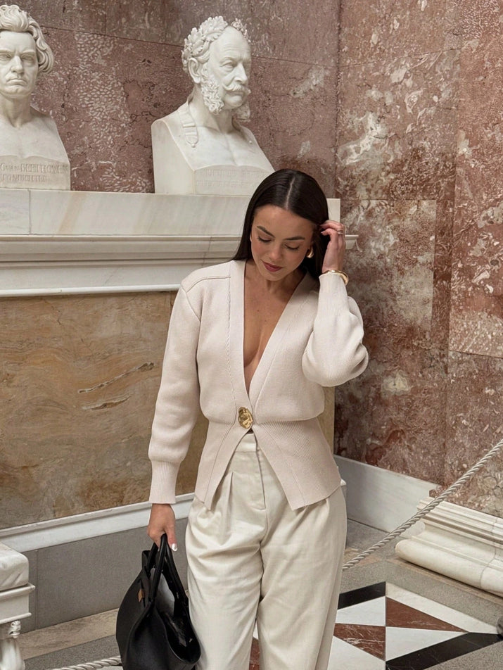 Model wearing a V-neck knit cardigan over a white tank top and trousers, enjoying a coffee outdoors in spring.