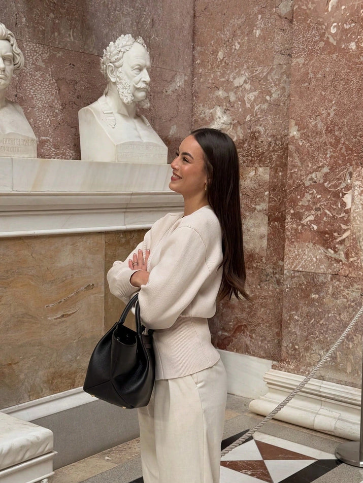 Model wearing a V-neck knit cardigan over a white tank top and trousers, enjoying a coffee outdoors in spring.