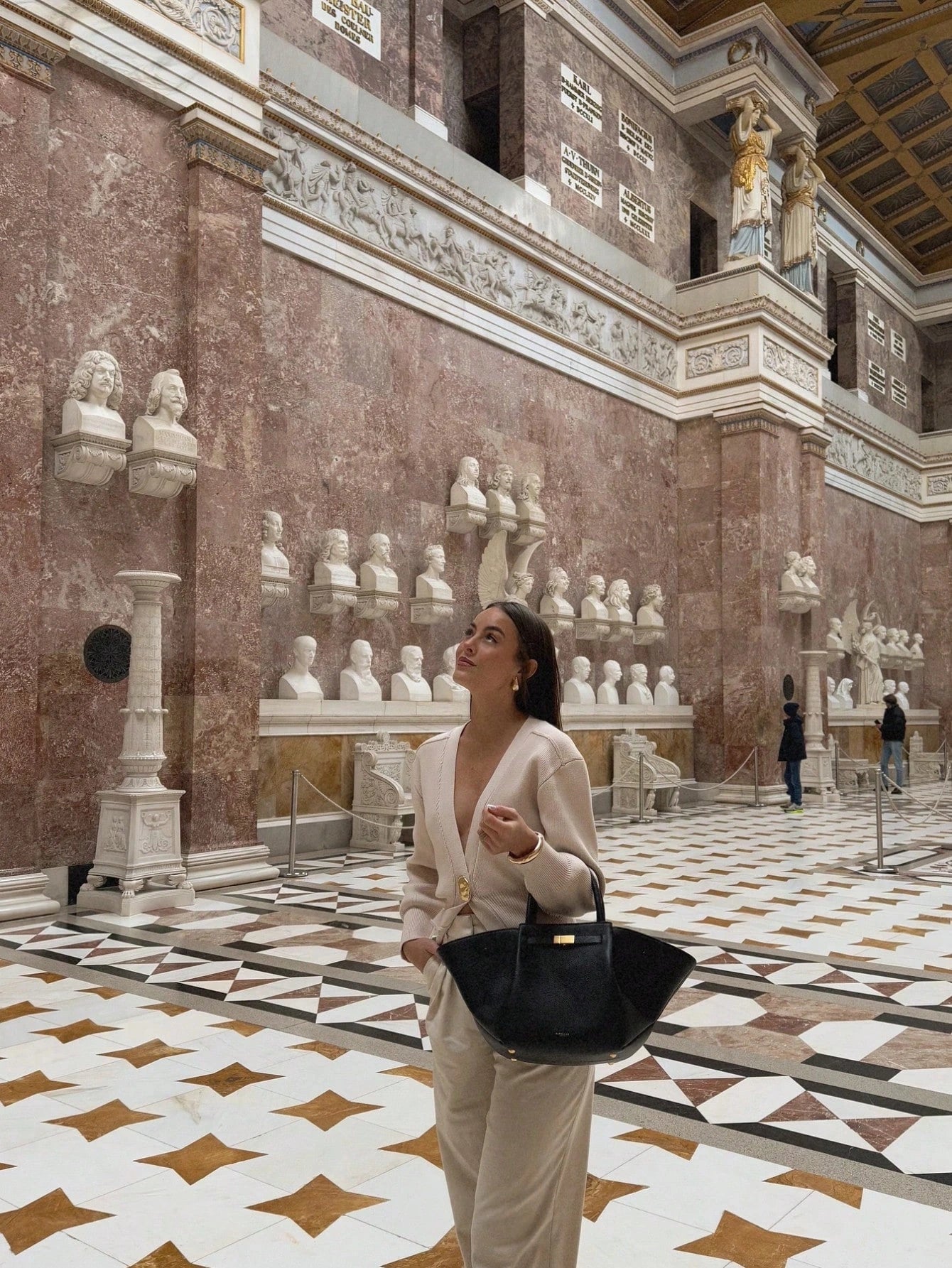 Model wearing a V-neck knit cardigan over a white tank top and trousers, enjoying a coffee outdoors in spring.