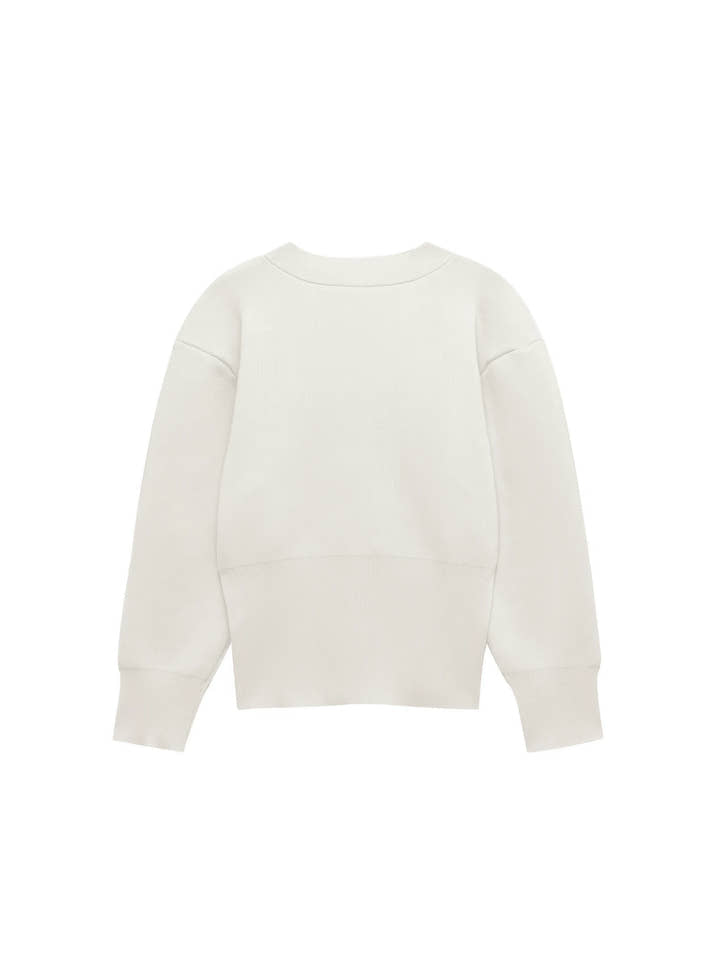 Model wearing a V-neck knit cardigan over a white tank top and trousers, enjoying a coffee outdoors in spring.